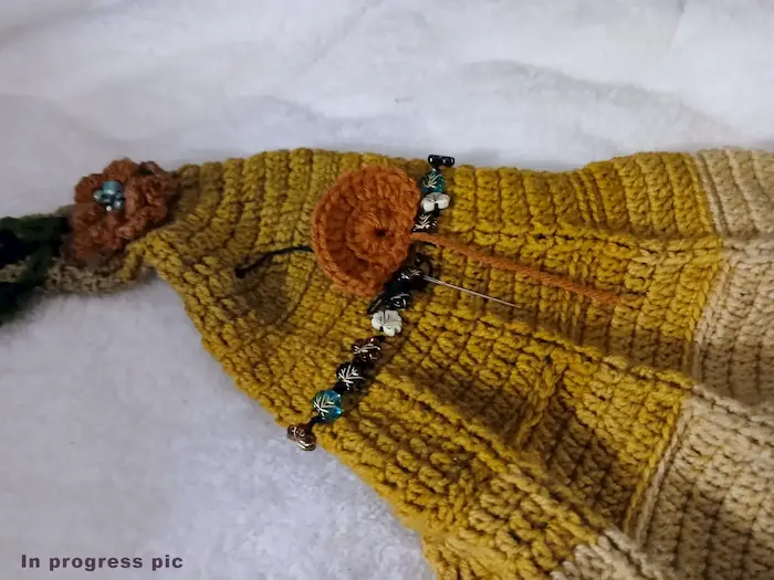 Handmade crochet elf hat in progress with bead embellishments and floral detail in earthy tones