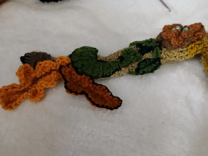 Close-up of handmade crochet elf hat scarf detail with textured leaves and floral accents in earthy tones