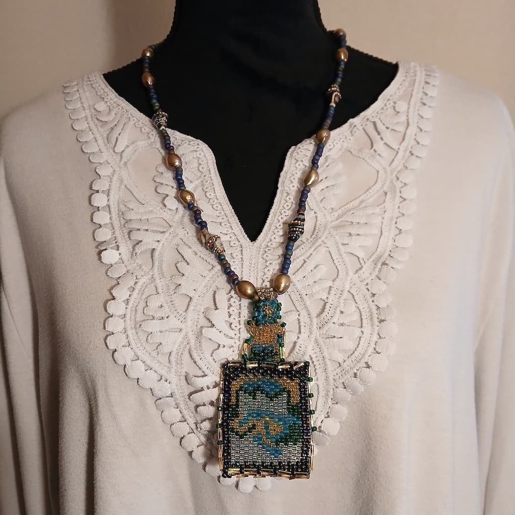 Handcrafted Beaded Water Fae Jewelry pendant necklace featuring an intricate rectangular beaded tapestry pendant with swirling ocean blue, green, gold, and silver seed beads, suspended from a matching beaded chain accented with large golden baroque pearls and metallic spacer beads, perfect as a unique Renaissance Faire necklace.
