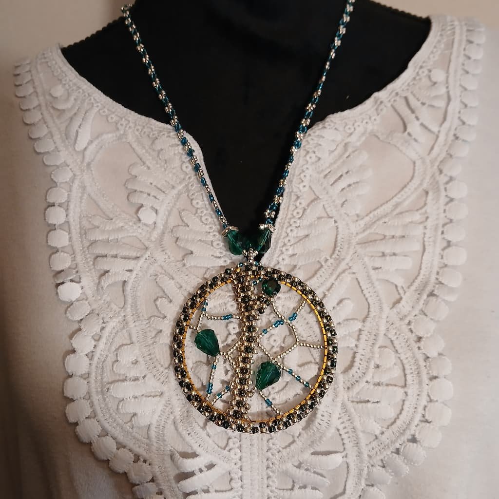 Green and gold circular pendant necklace resting on a white lace blouse